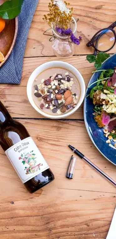 Plateau-repas : salade composée, bol de granola et cidre bio sur une table en bois
