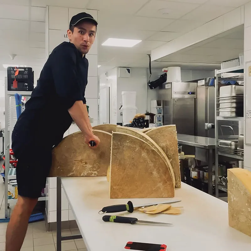 Un cuisinier du Moulin découpe une meule de fromage